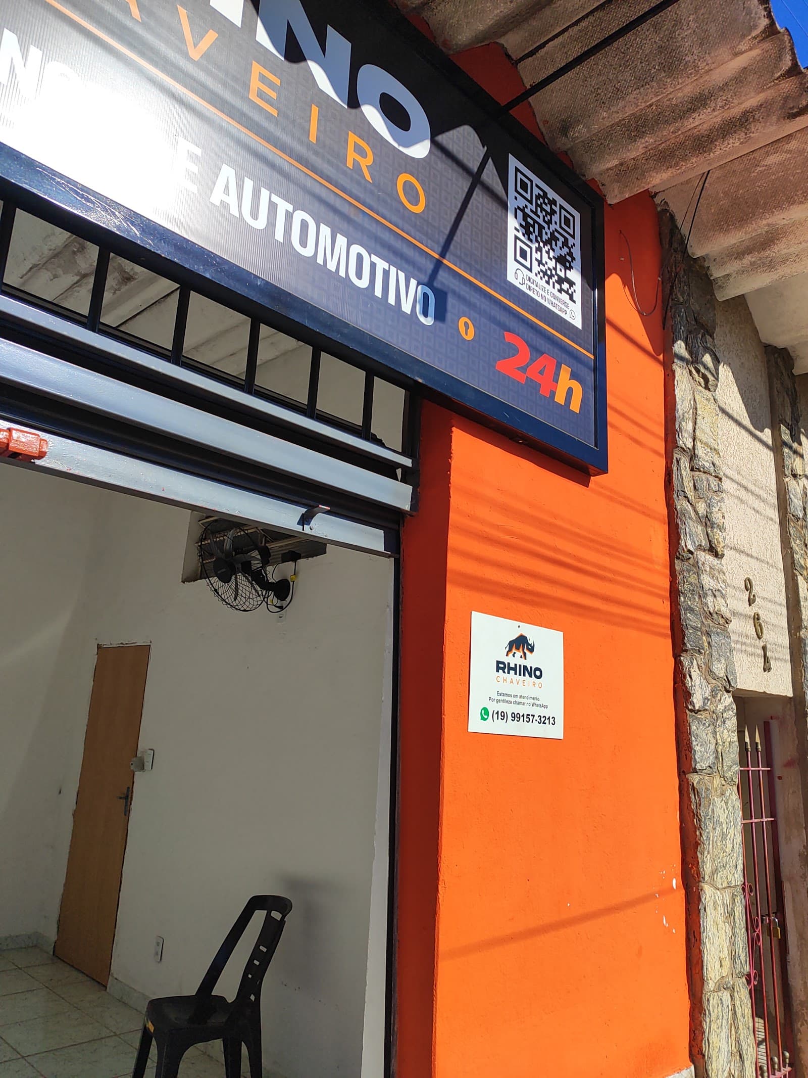 Parede laranja da loja com a plaquinha: estamos em atendimento, por gentileza chamar no WhatsApp (19) 99157-3213, e o número 264 ao lado